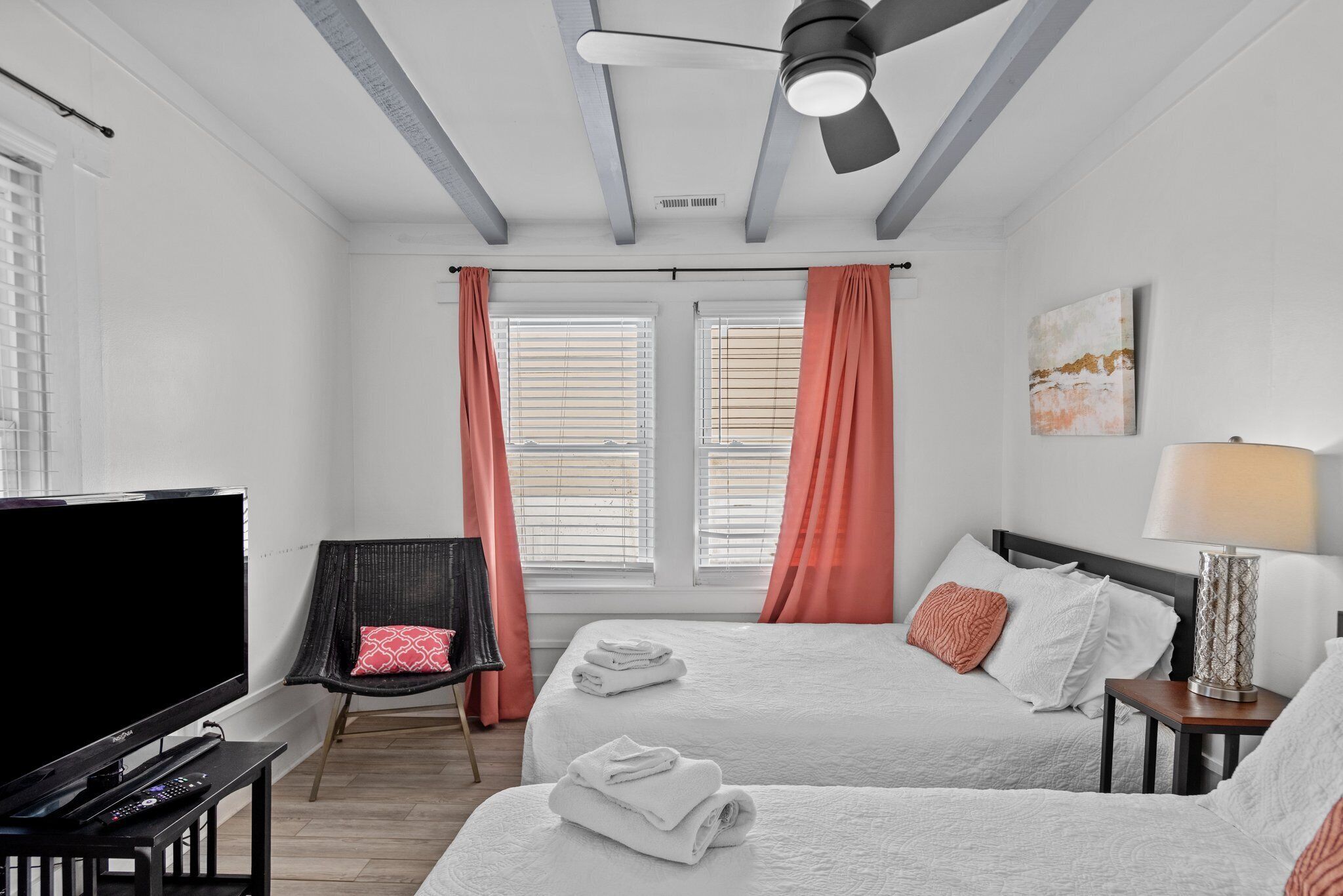 A hotel room with two beds, a TV, a chair, and a ceiling fan.