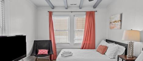A hotel room with two beds, a TV, a chair, and a ceiling fan.