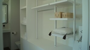 Un baño con repisas blancas, un inodoro y un espejo.
