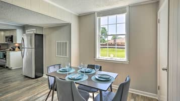 Un coin repas avec une table dressée pour quatre personnes, une cuisine en arrière-plan et une fenêtre donnant sur une cour.