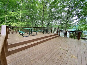 Een houten terras met picknicktafels en een hek, uitkijkend op een wateroppervlak.