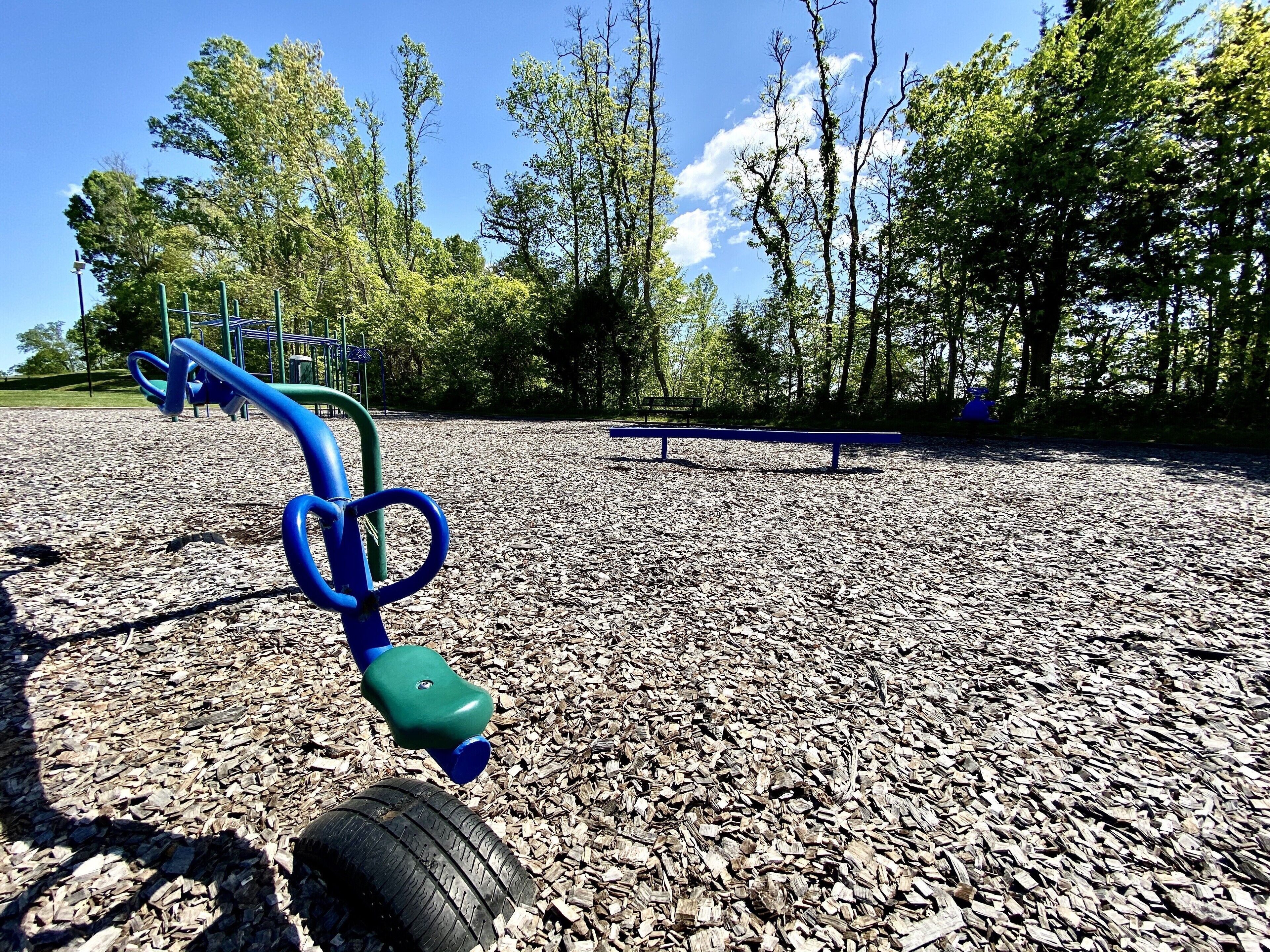 A playground with a blue and green play structure, a rubberized ground surface, and a bench in the background.