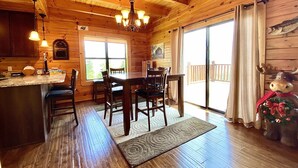 Interior de una cabaña de madera con comedor, cocina y un ventanal grande.