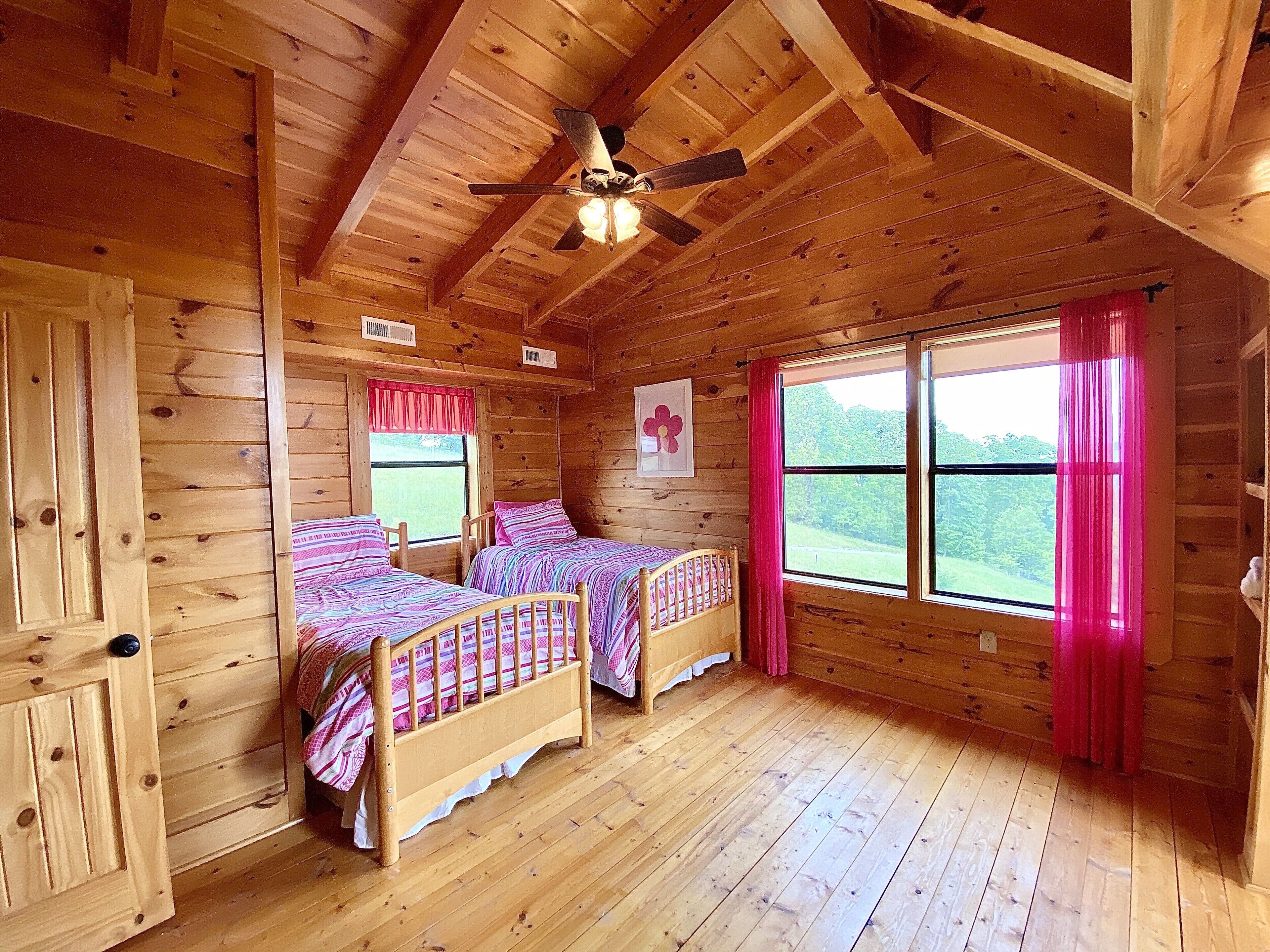 Una cabaña con dos camas de madera, un ventilador de techo y una ventana con vistas al exterior.