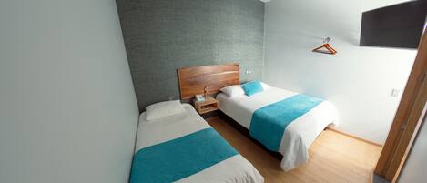 Een moderne hotelkamer met twee eenpersoonsbedden, een houten hoofdbord, een nachtkastje met een telefoon en een aan de muur bevestigde televisie.