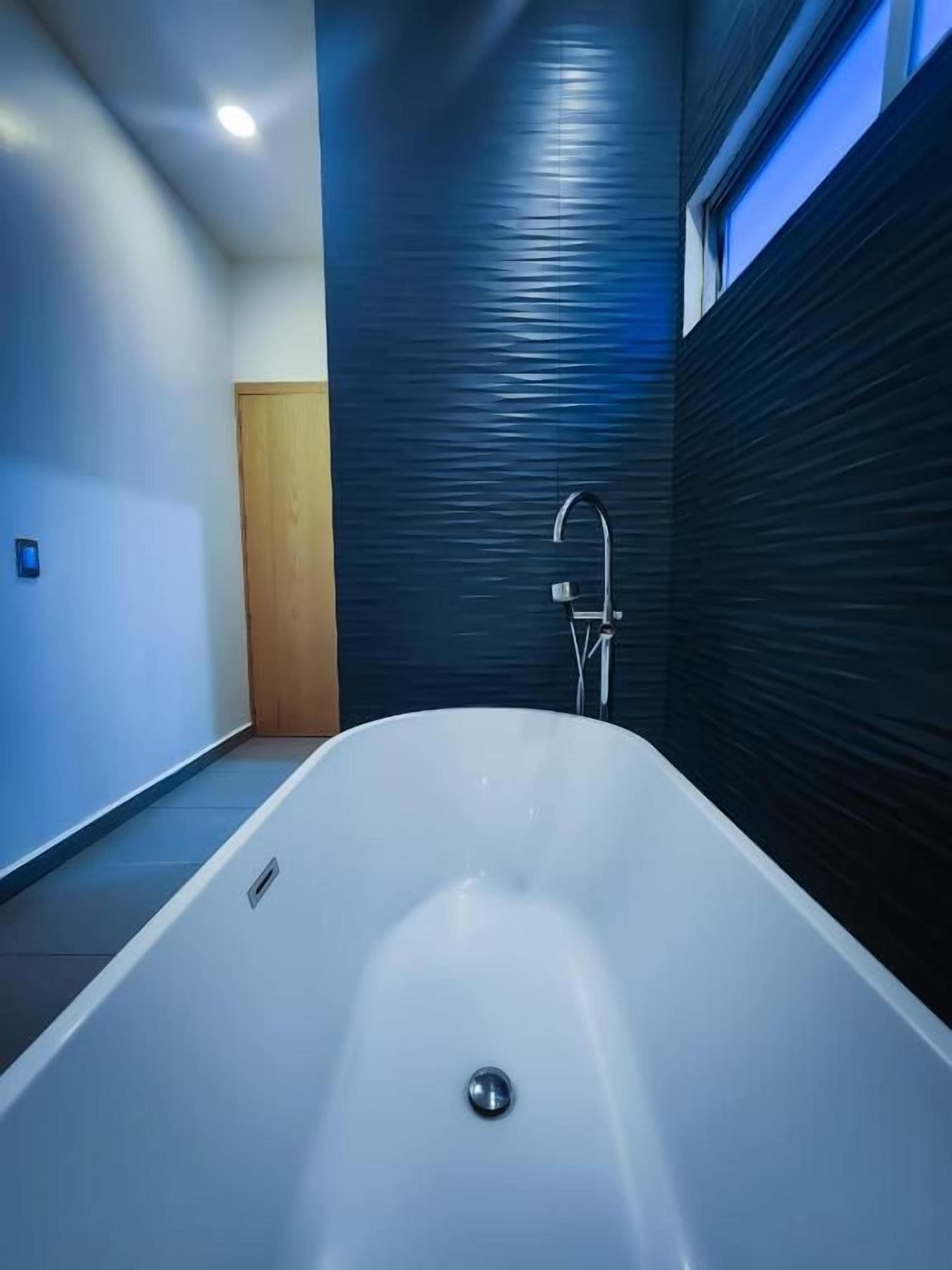 A modern bathroom with a freestanding bathtub, a wall-mounted faucet, and a window providing natural light.