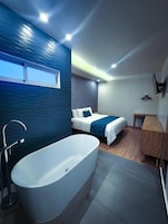 Un baño moderno con una bañera independiente, zona de ducha y una mesita de noche.