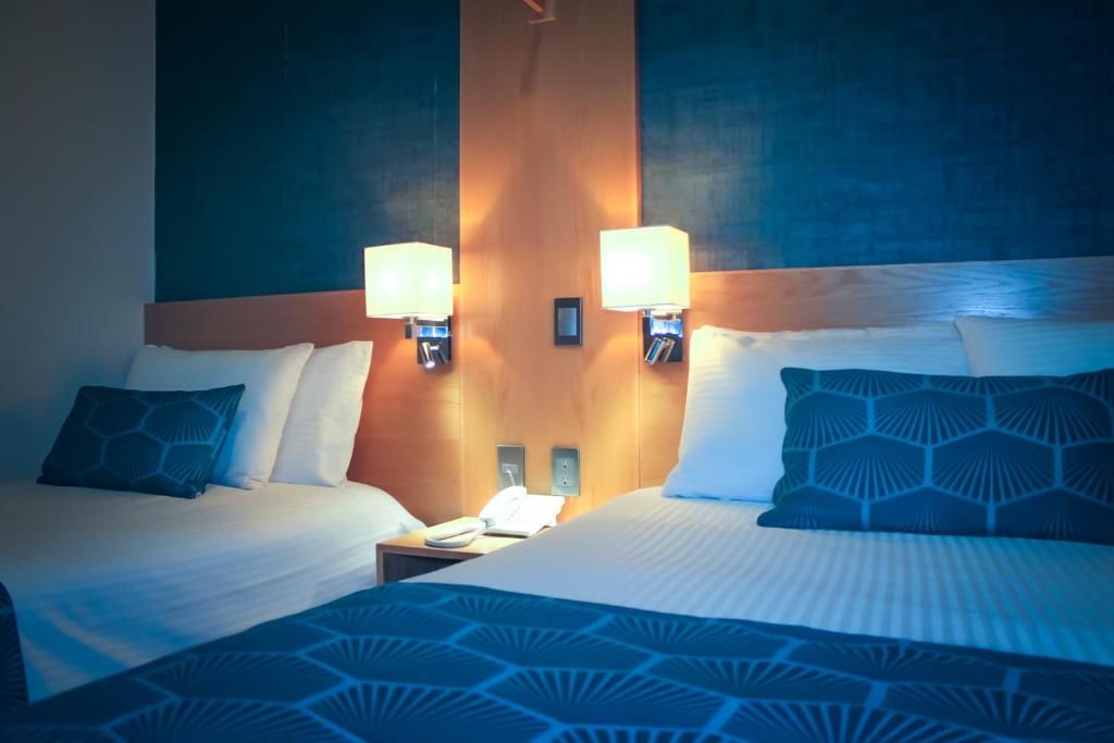 Una habitación de hotel con dos camas, una mesita de noche con teléfono y lámparas de pared.