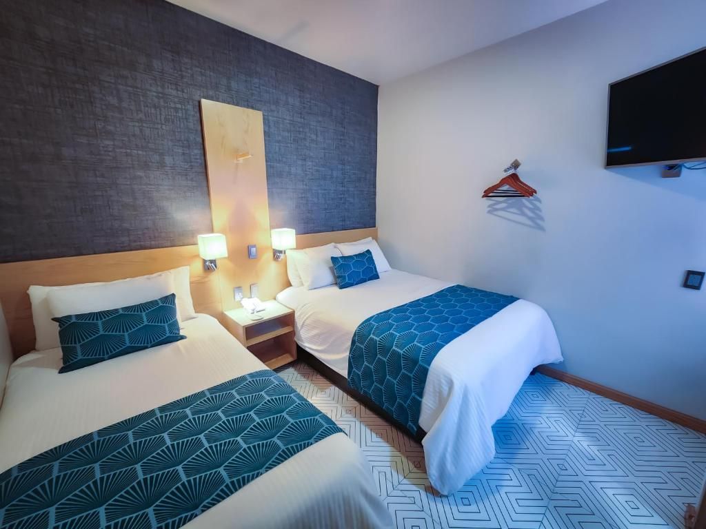 Habitación de hotel con dos camas, un televisor, un perchero y una lámpara fijada a la pared.