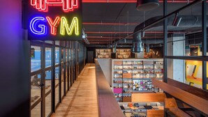 A modern gym interior with a neon sign, wooden flooring, and a variety of fitness equipment. - Moxy Lisboa Oriente (Lisbon)