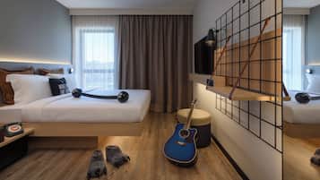A modern hotel room with a bed, a guitar, a small stool, and a TV mounted on a grid wall.
