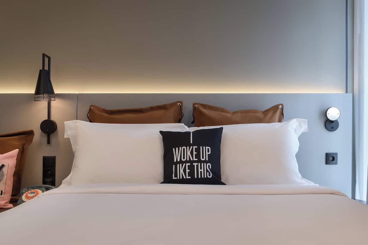 A neatly made bed with a pillow that reads "I woke up like this."