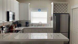 A modern kitchen with white cabinets, a stainless steel refrigerator, and a large island with bar stools. - Close to Seaside! Cozy Cottage. Private heated pool  (Santa Rosa Beach)