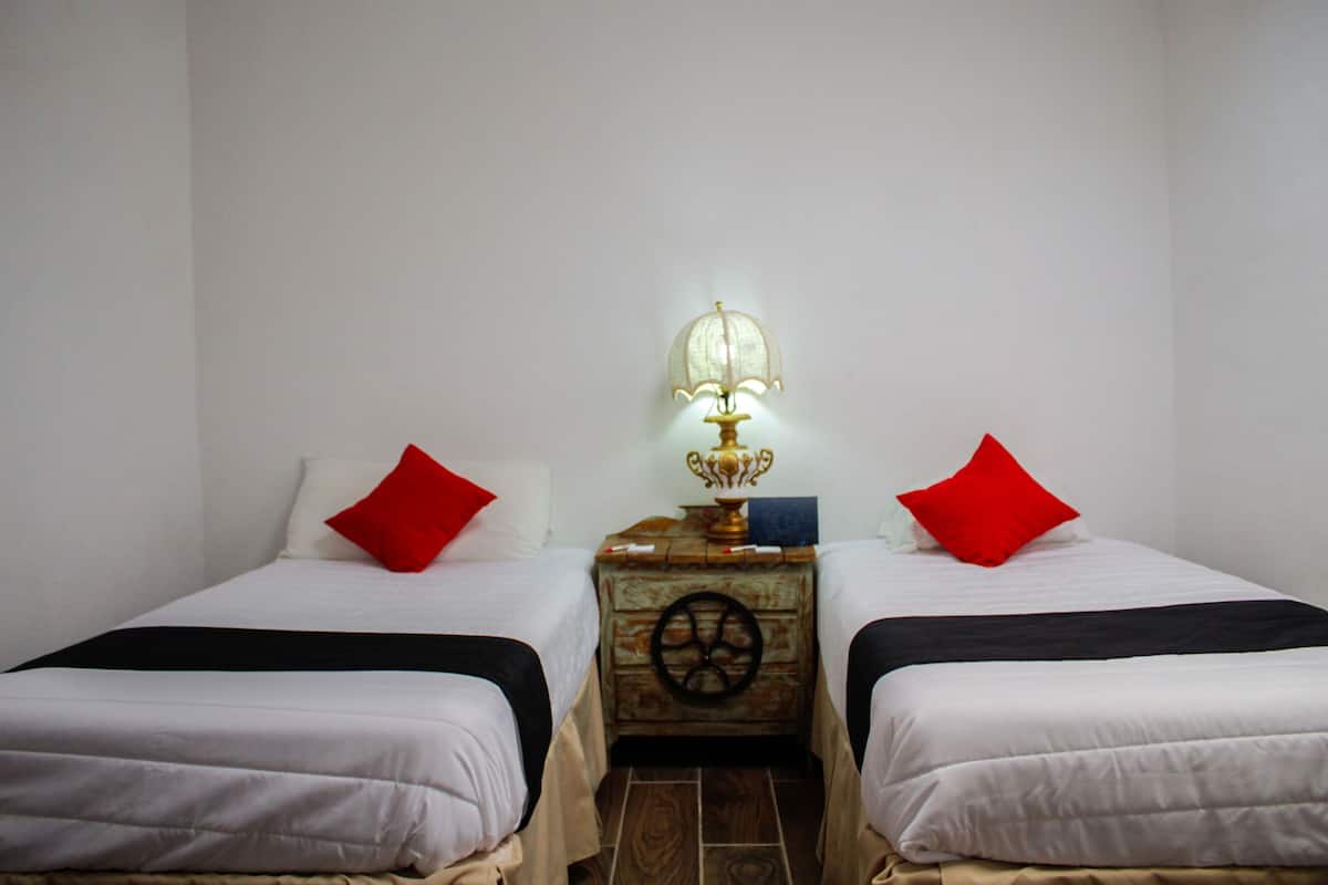 Een kamer met twee bedden, elk voorzien van een rood kussen, een klein tafeltje met een lamp, en een decoratief wiel aan de muur.