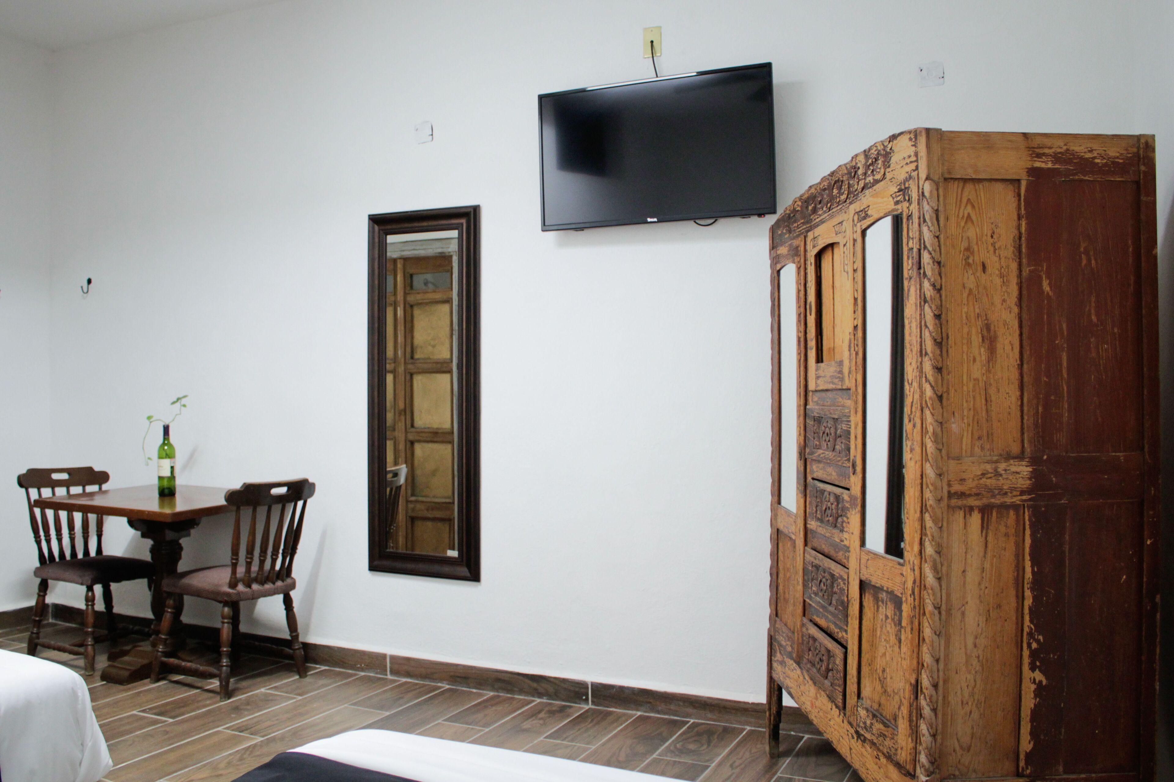 A room with a wooden cabinet, a television mounted on the wall, a wooden door, and a dining table with chairs.