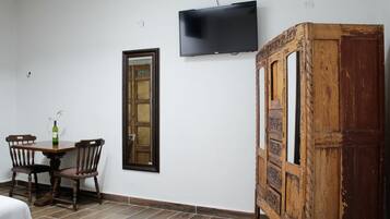 A room with a wooden cabinet, a television mounted on the wall, a wooden door, and a dining table with chairs.