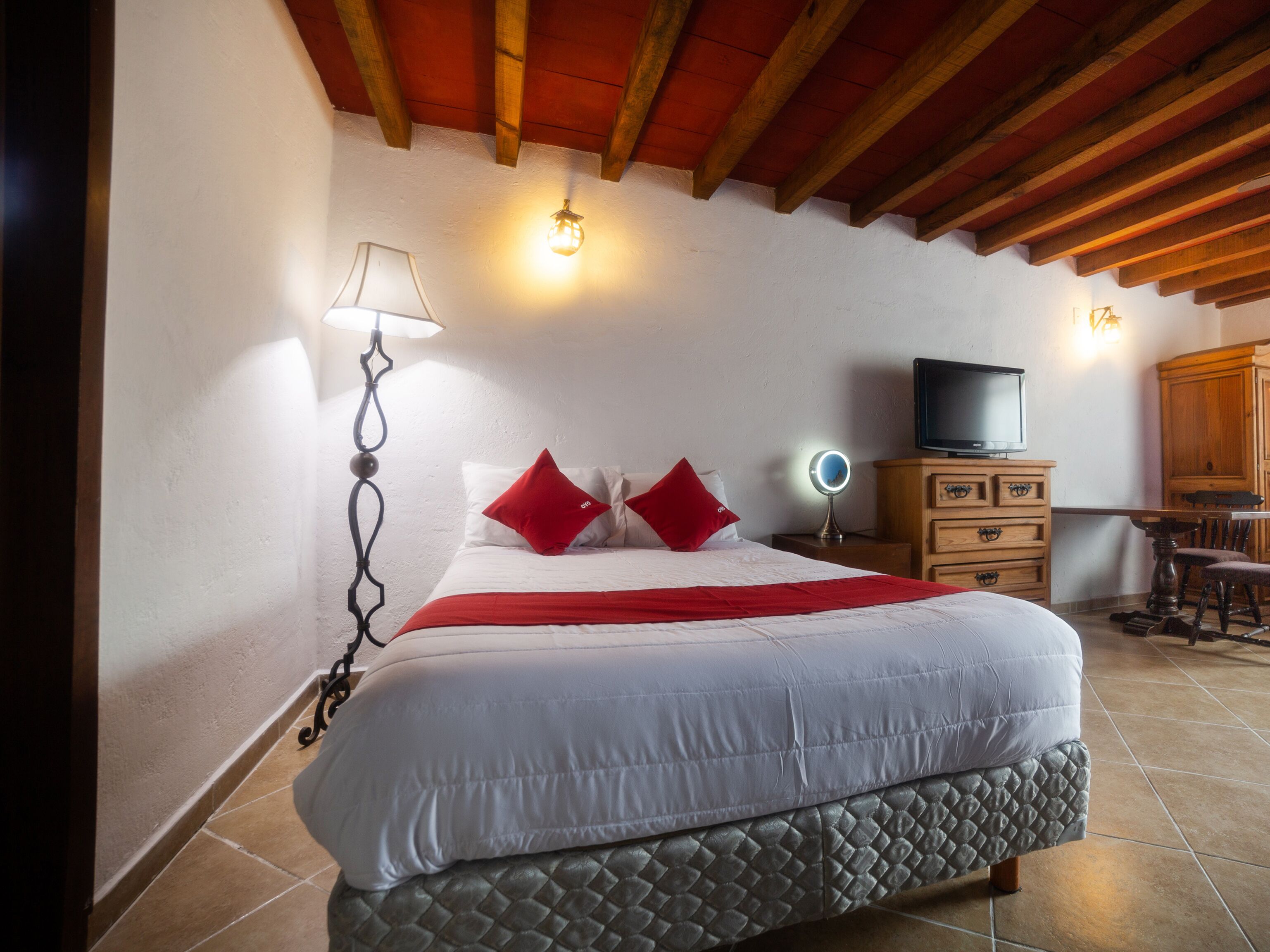 A bedroom with a large bed, a bedside table with a lamp, a TV, and a wooden cabinet.