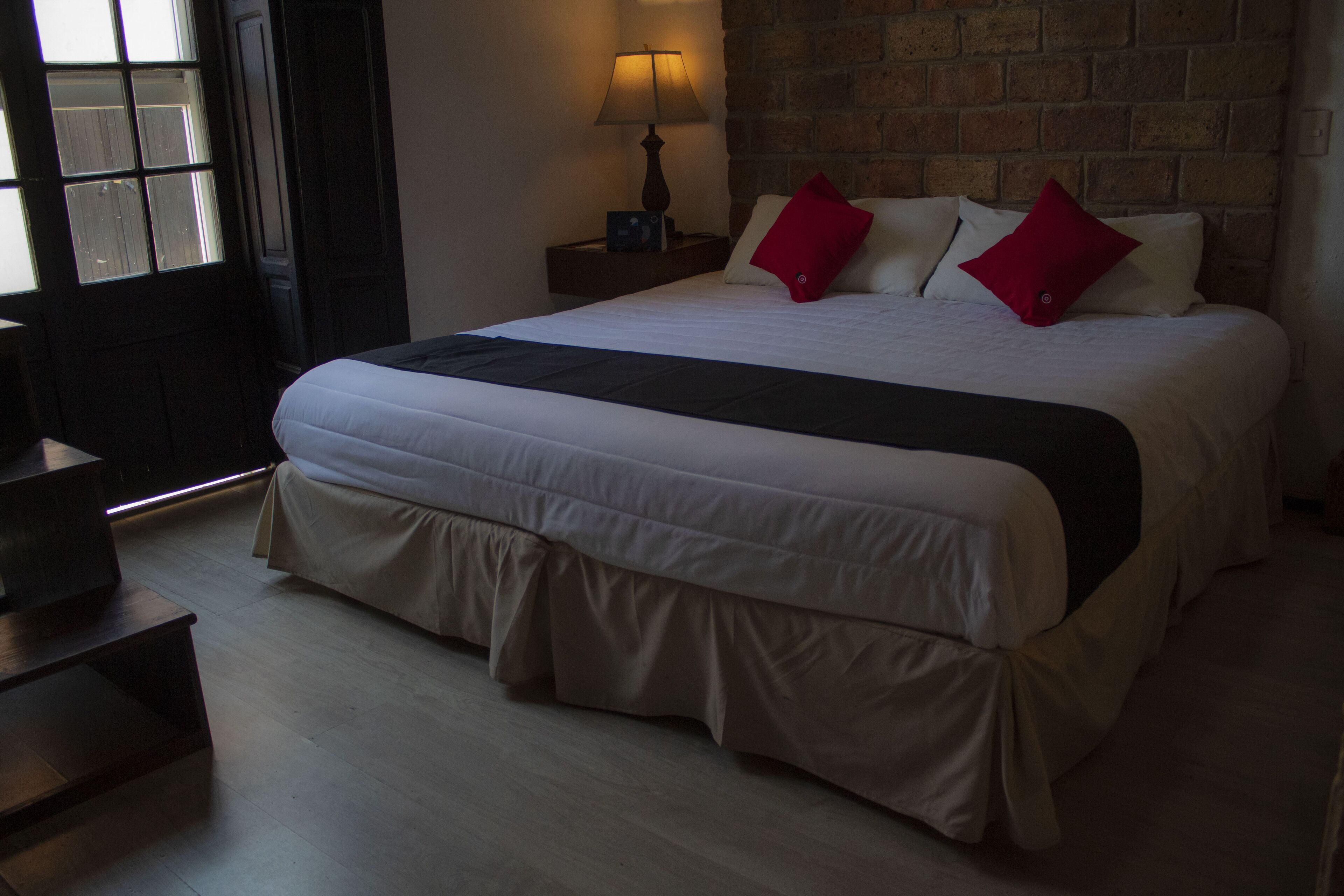 A neatly made bed with a white and black bedspread, two red pillows, and a wooden nightstand with a lamp.