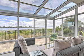 Un solárium con techo de vidrio, vistas a un lago y una zona de estar con mesa y sillas.