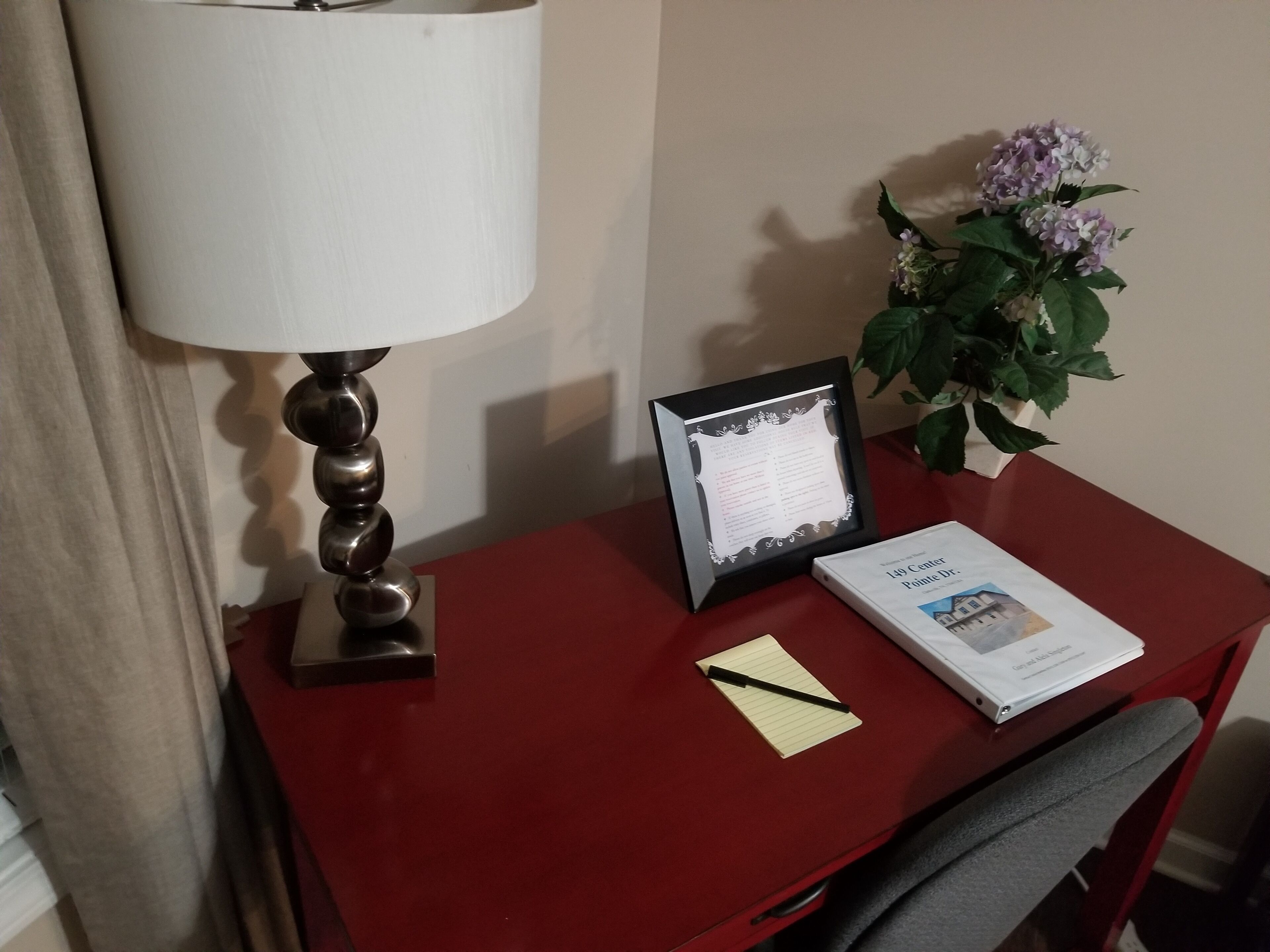 Een bureau met een lamp, een lijst met een document, een notitieboek, een boek en een kamerplant.