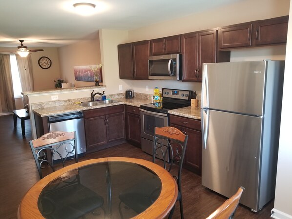 A modern kitchen with dark wood cabinets, stainless steel appliances, and a glass-top dining table.