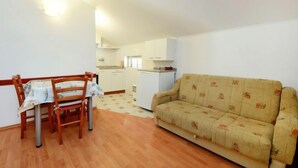 A compact living space with a dining table and chairs, a sofa, a kitchenette, and a small refrigerator.