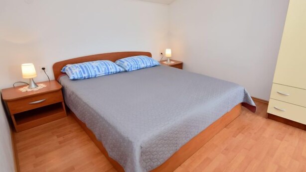 A bedroom with a single bed, two bedside tables with lamps, a wooden nightstand, and a wardrobe.