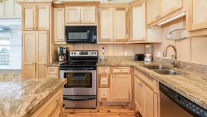 A kitchen with wooden cabinets, a microwave, a stove, a sink, and a dishwasher. - Laguna Harbor Cottage (Bolivar Peninsula)