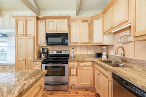 A kitchen with wooden cabinets, a microwave, a stove, a sink, and a dishwasher. - Laguna Harbor Cottage (Bolivar Peninsula)