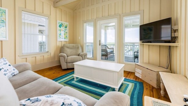 A cozy living room with a white sofa, a beige armchair, a white coffee table, and a TV on a wooden stand. - Laguna Harbor Cottage (Bolivar Peninsula)