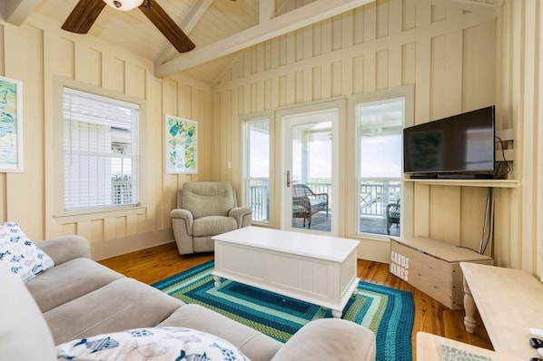 A cozy living room with a white sofa, a beige armchair, a white coffee table, and a TV on a wooden stand. - Laguna Harbor Cottage (Bolivar Peninsula)