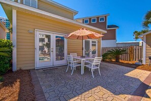 A patio with a table and chairs, a patterned umbrella, and a wooden fence. - Happy Ours (Panama City Beach)