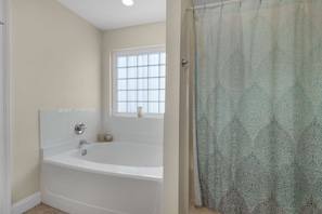 A bathroom with a white bathtub, a window, and a patterned shower curtain. - Happy Ours (Panama City Beach)