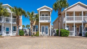 A row of beachfront condominiums with balconies, palm trees, and a paved walkway. - Happy Ours (Panama City Beach)