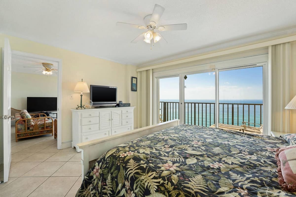 Une chambre à coucher comprenant un lit, une télévision, une commode et un balcon avec vue sur l’océan.