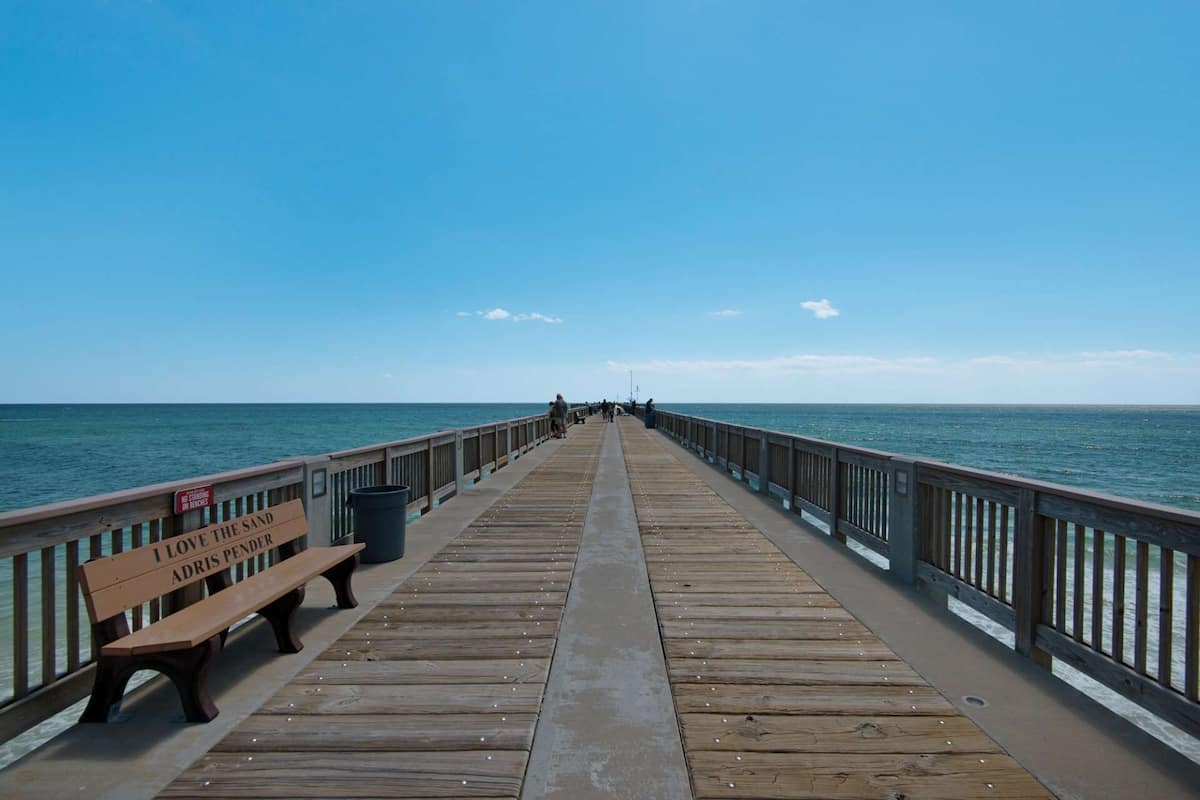 Une jetée en bois s’étendant dans l’océan, avec un banc et une pancarte sur laquelle on peut lire : « J’AIME LE SABLON ADRIS PENDER ».