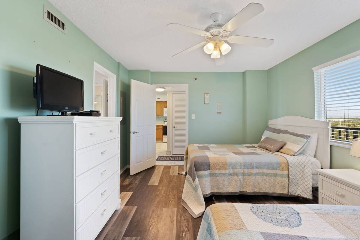 Une chambre à coucher avec un lit, une télévision, une commode et un ventilateur de plafond.