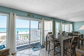 A dining area with a view of the beach, a balcony with a railing, and a door leading outside. - Emerald Winds (Panama City Beach)
