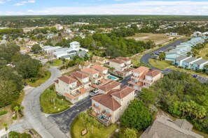 An aerial view of a residential area with multiple two-story houses, a central road, and surrounding greenery. - All Decked Out - 140 Southfield (Panama City Beach)