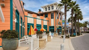 A hotel with a colorful facade, outdoor seating with umbrellas, and palm trees.