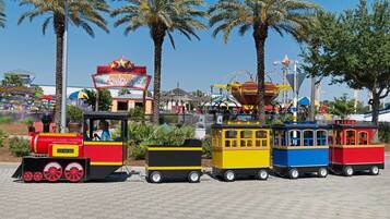 A miniature train ride with colorful carriages, a Ferris wheel, and palm trees in the background.