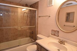 A bathroom with a glass-enclosed shower, a toilet, a sink with a mirror, and a towel rack.