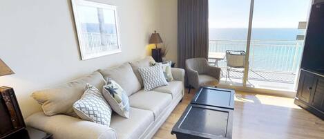 Una sala de estar con sofá, sillones, una mesa de centro y un balcón con vistas al mar.