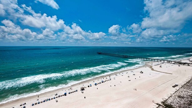 Een strand met een pier die zich uitstrekt in de oceaan, zandstrand en helderblauwe lucht.