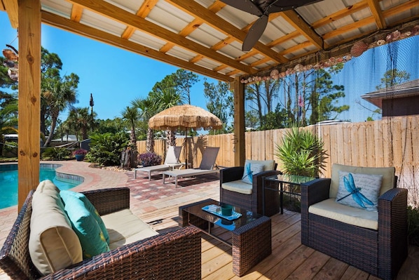 A covered outdoor patio with wicker furniture, a pool, and a thatched umbrella.