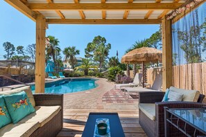 A pool area with lounge chairs, a thatched umbrella, and a wooden pergola. - Tickled Turtle Beach House (Panama City Beach)