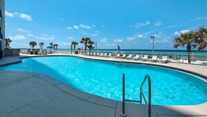 A swimming pool with a curved edge, surrounded by lounge chairs and palm trees, with a clear view of the ocean in the background. - Watercrest by iTrip Panama City Beach (Panama City Beach)
