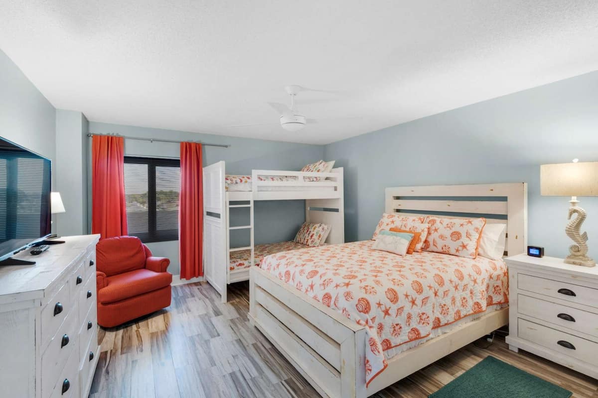 A bedroom with bunk beds, a desk with a chair, a TV, and a lamp.