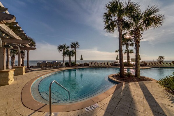 Area piscina con lettini, palme e vista sull'oceano.