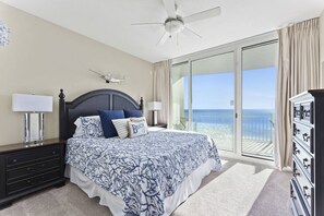 Una camera da letto con un letto, due comodini, una ventola a soffitto, un comò e vista sull'oceano tramite una porta scorrevole in vetro.